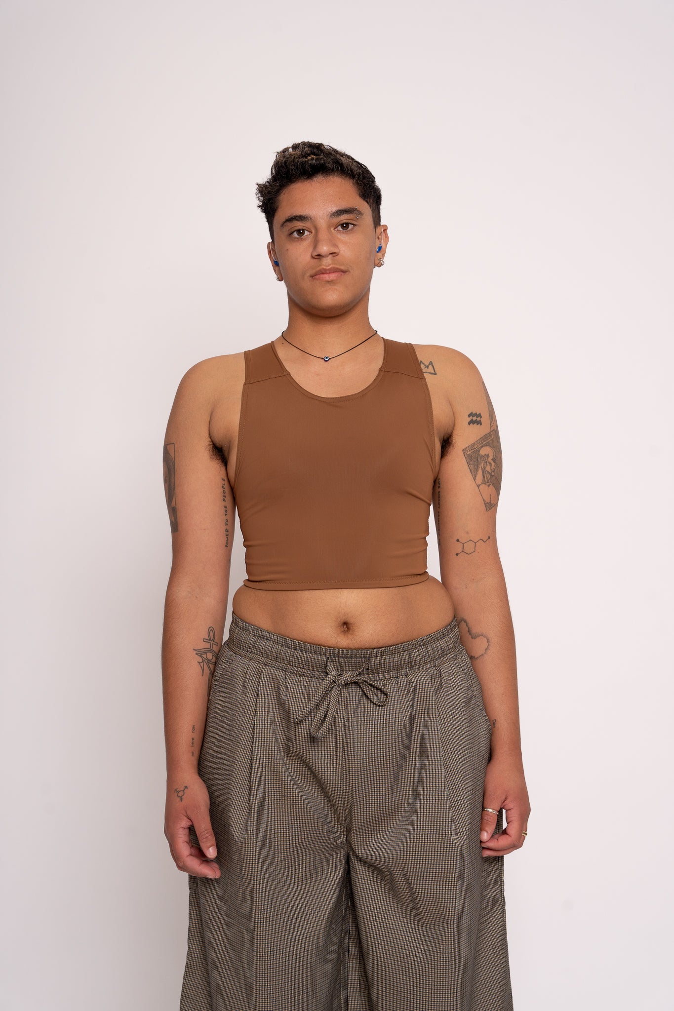 Person wearing a brown chest binder  and grey pants against a white background