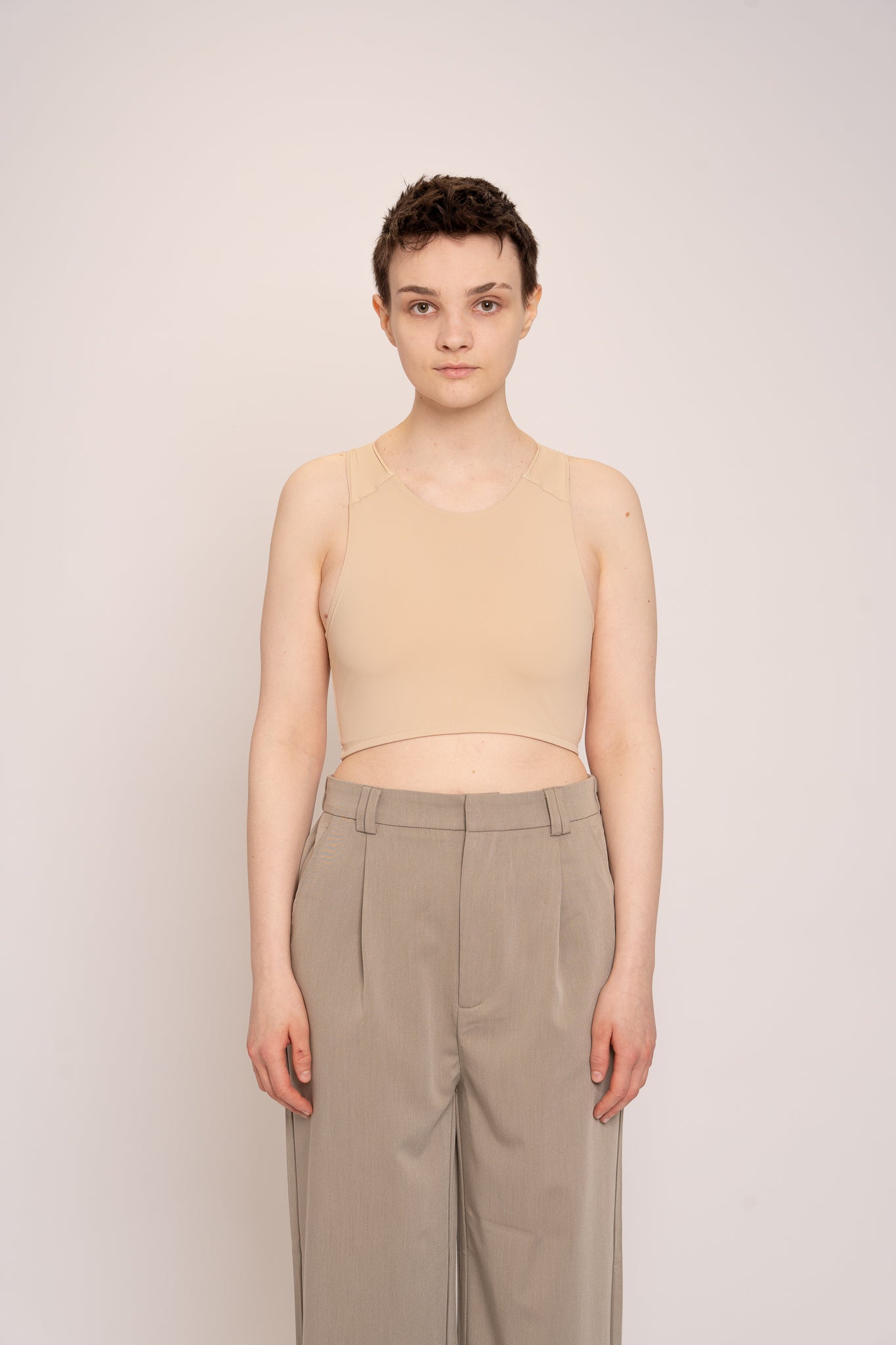 Person wearing a beige chest binder  and beige pants against a plain background