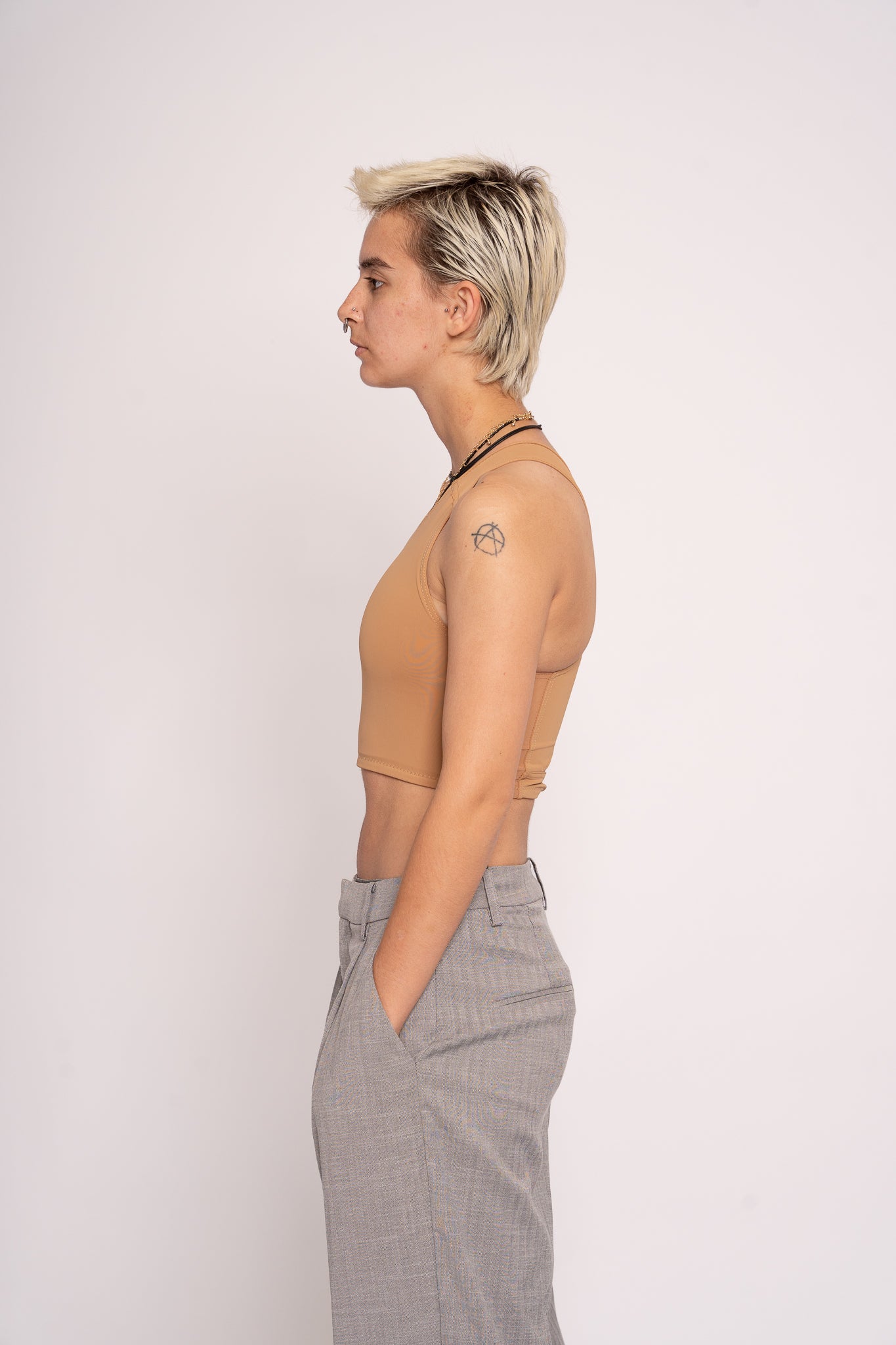 a person wearing a chest binder and grey trousers against a white background 