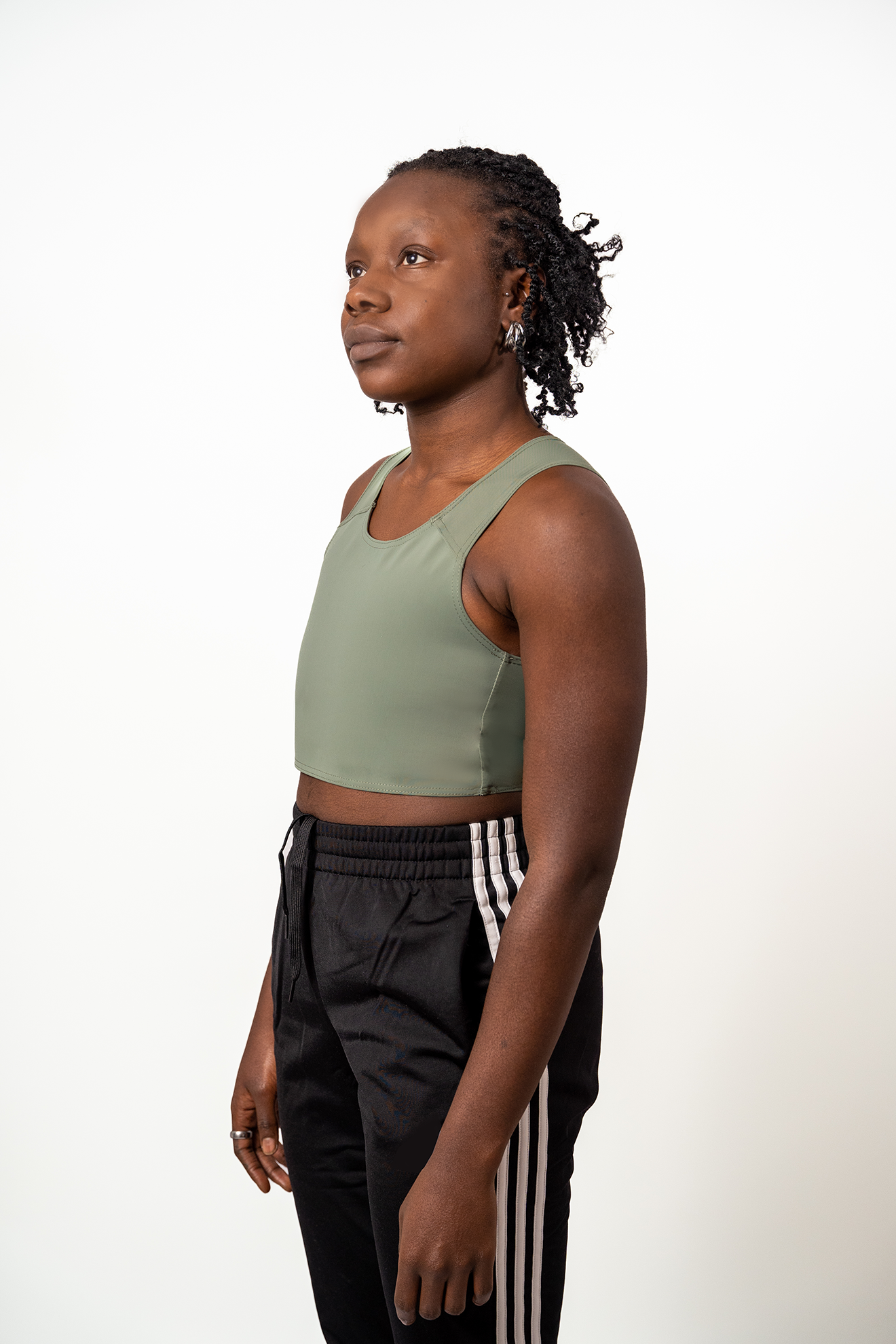 Person wearing a muted green short chest binder and black jogging bottoms with white stripes against a white background