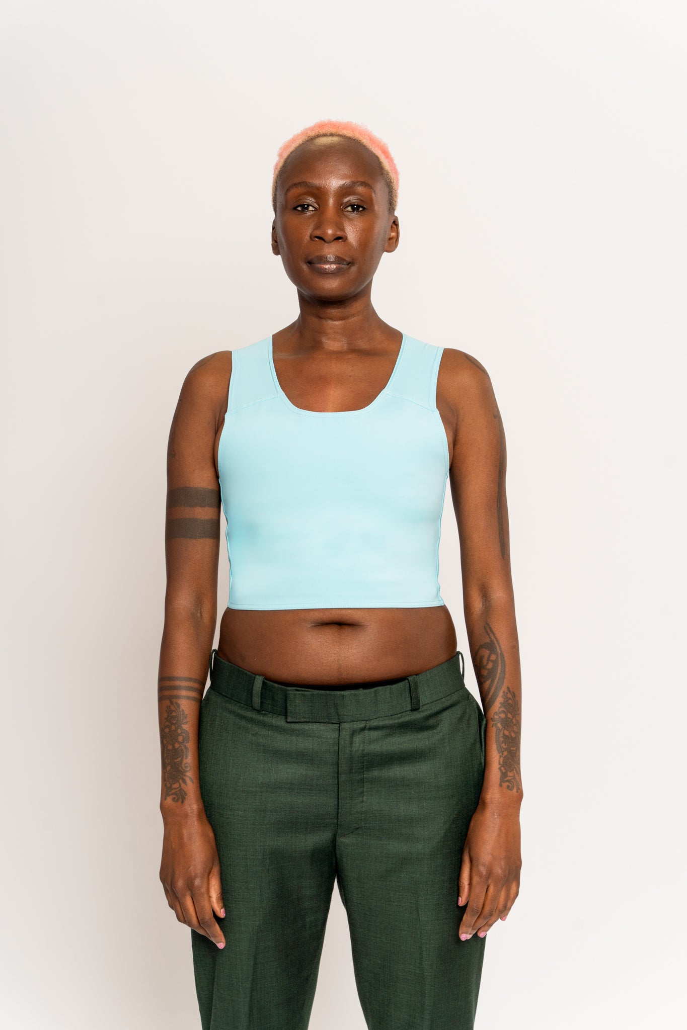 Person wearing a light blue coloured short chest binder and blue jeans with a black belt against a white background.