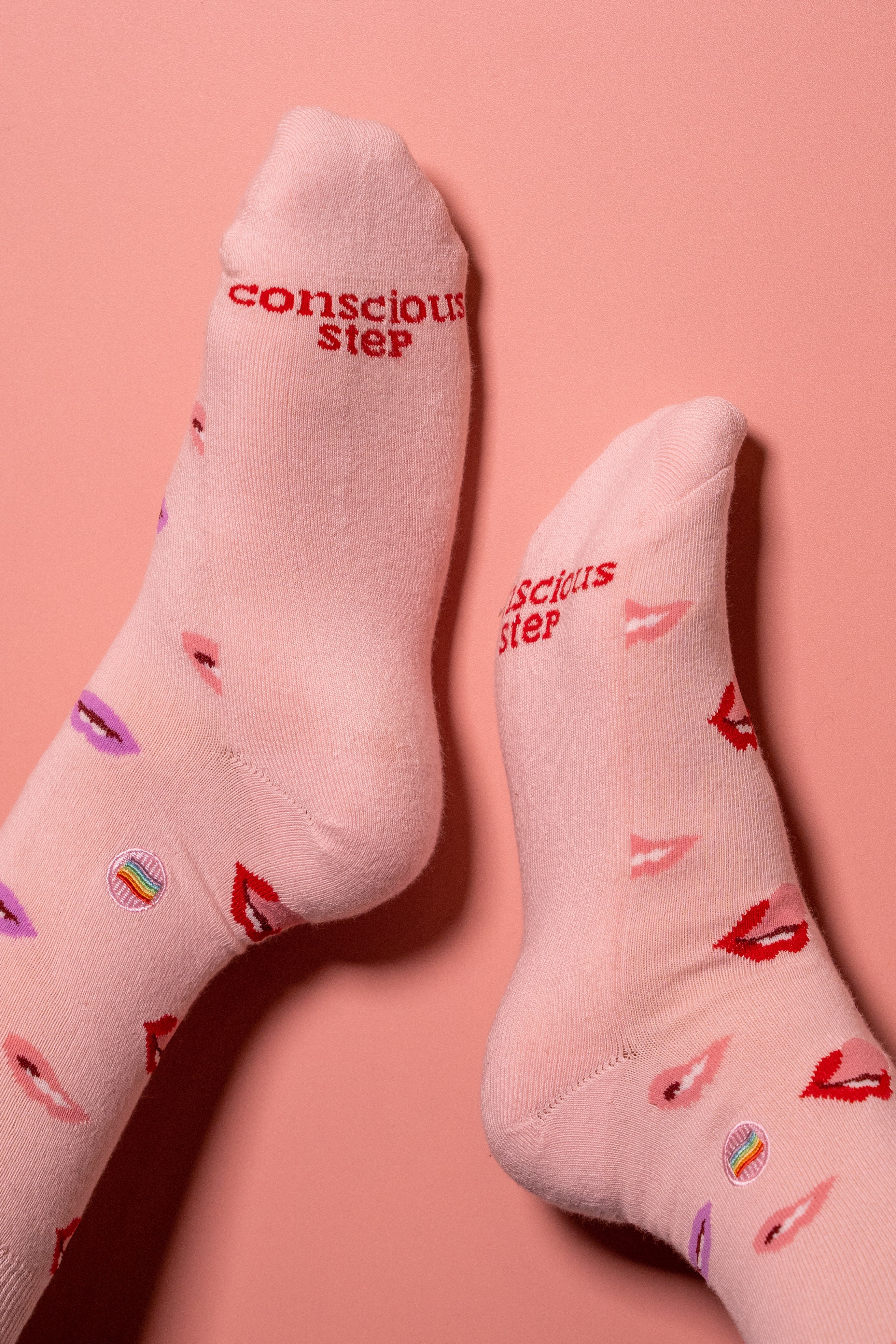 Pink socks with 'conscious step' text and lips design on a pink background