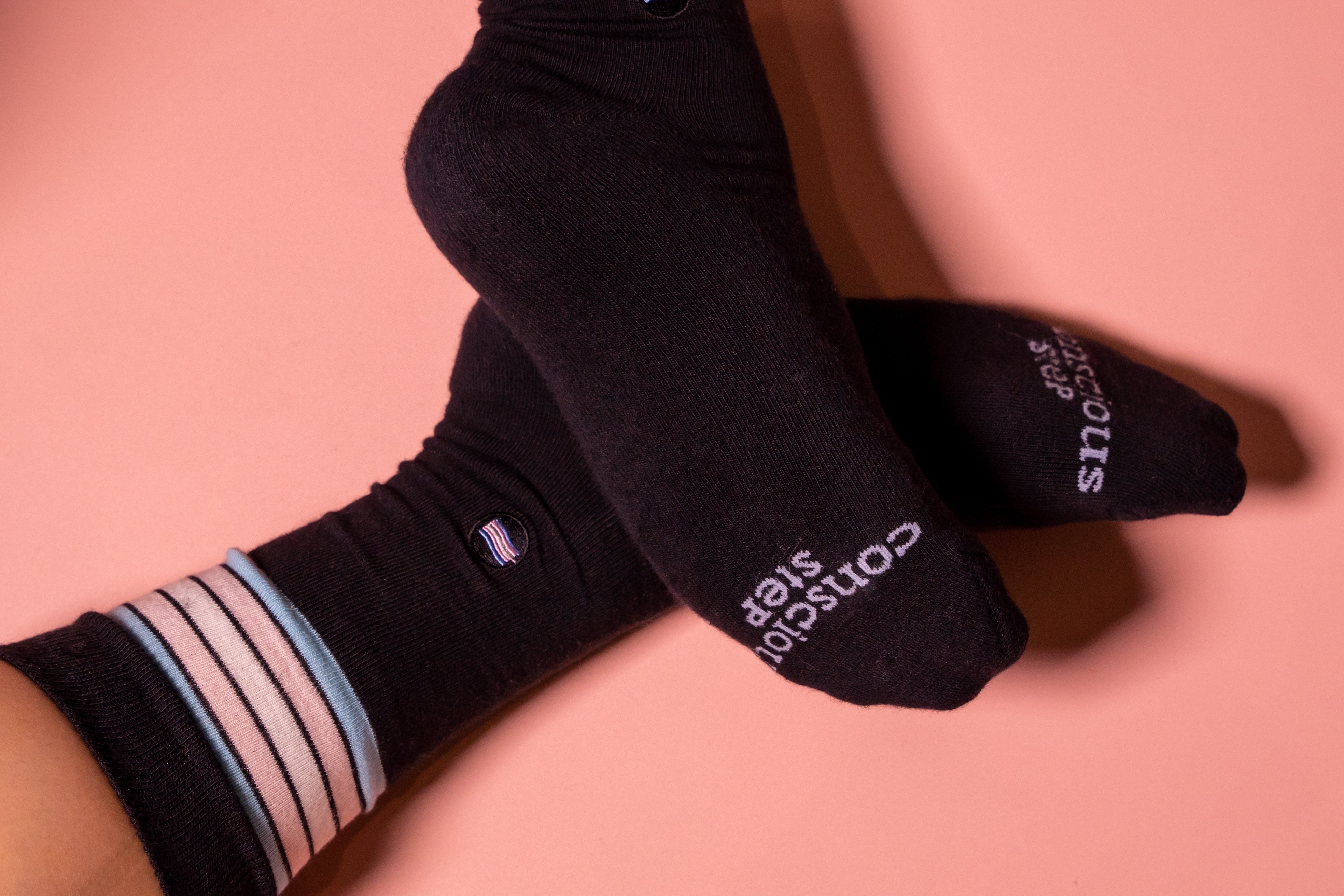 Black socks with striped trans flag coloured cuffs on a pink background