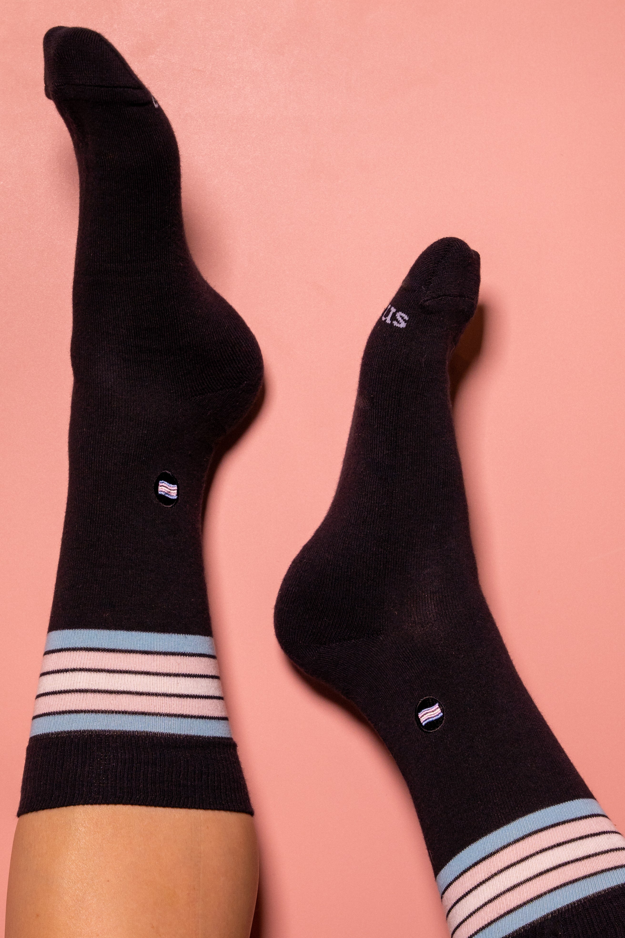 Black socks with striped pink, white and blue cuffs on a pink background