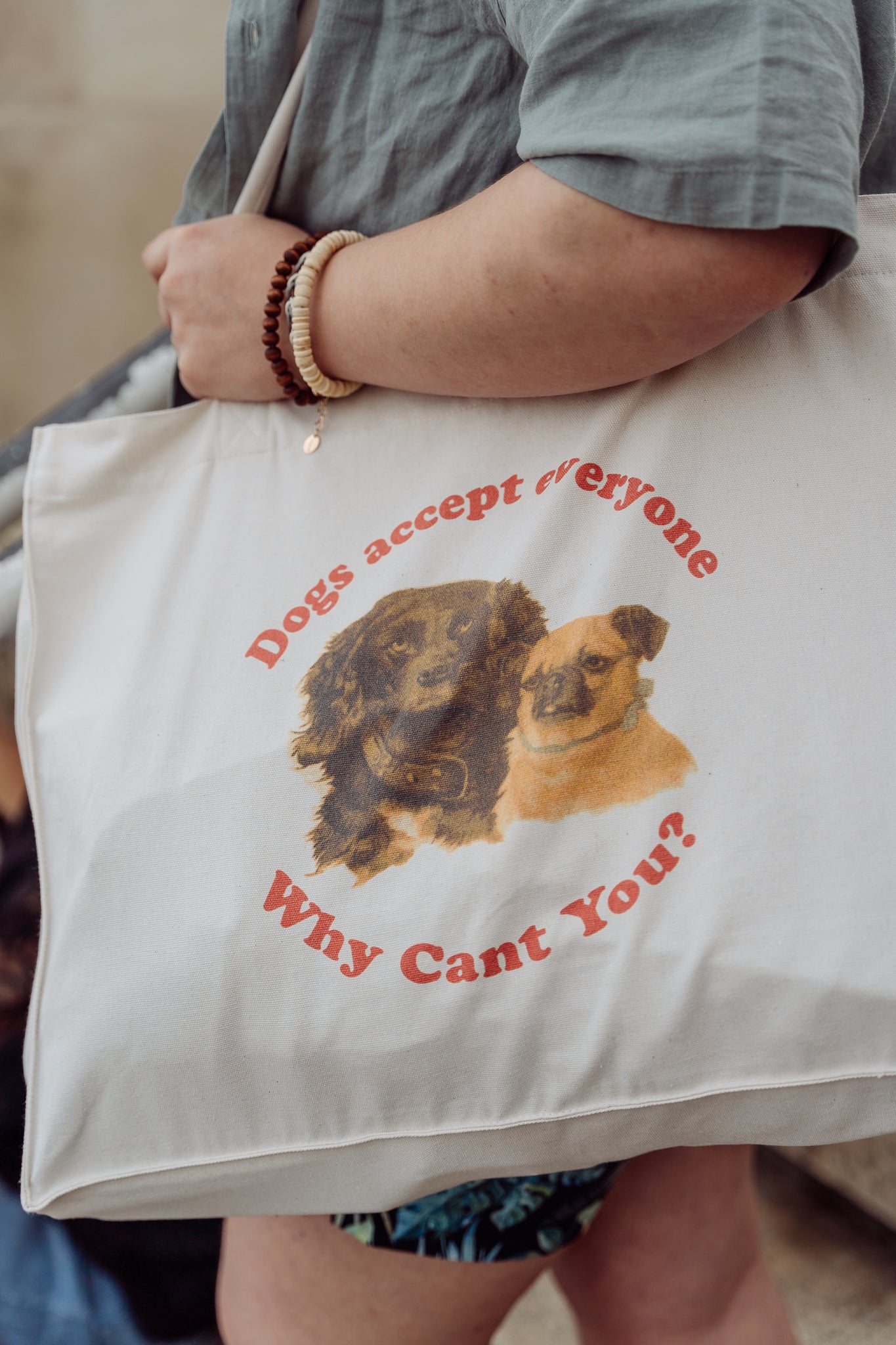 Tote bag with dog graphic and 'Dogs accept everyone why cant you' text held by a person. 