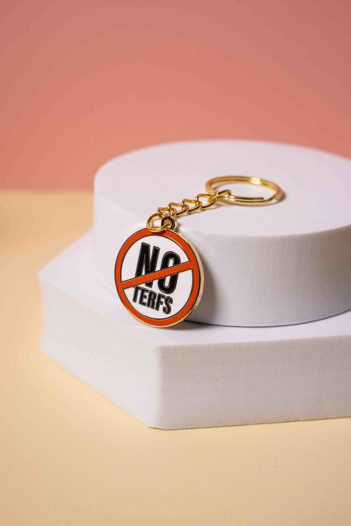 Keychain with 'No Terfs' design on a white box with a pinkish-orange background