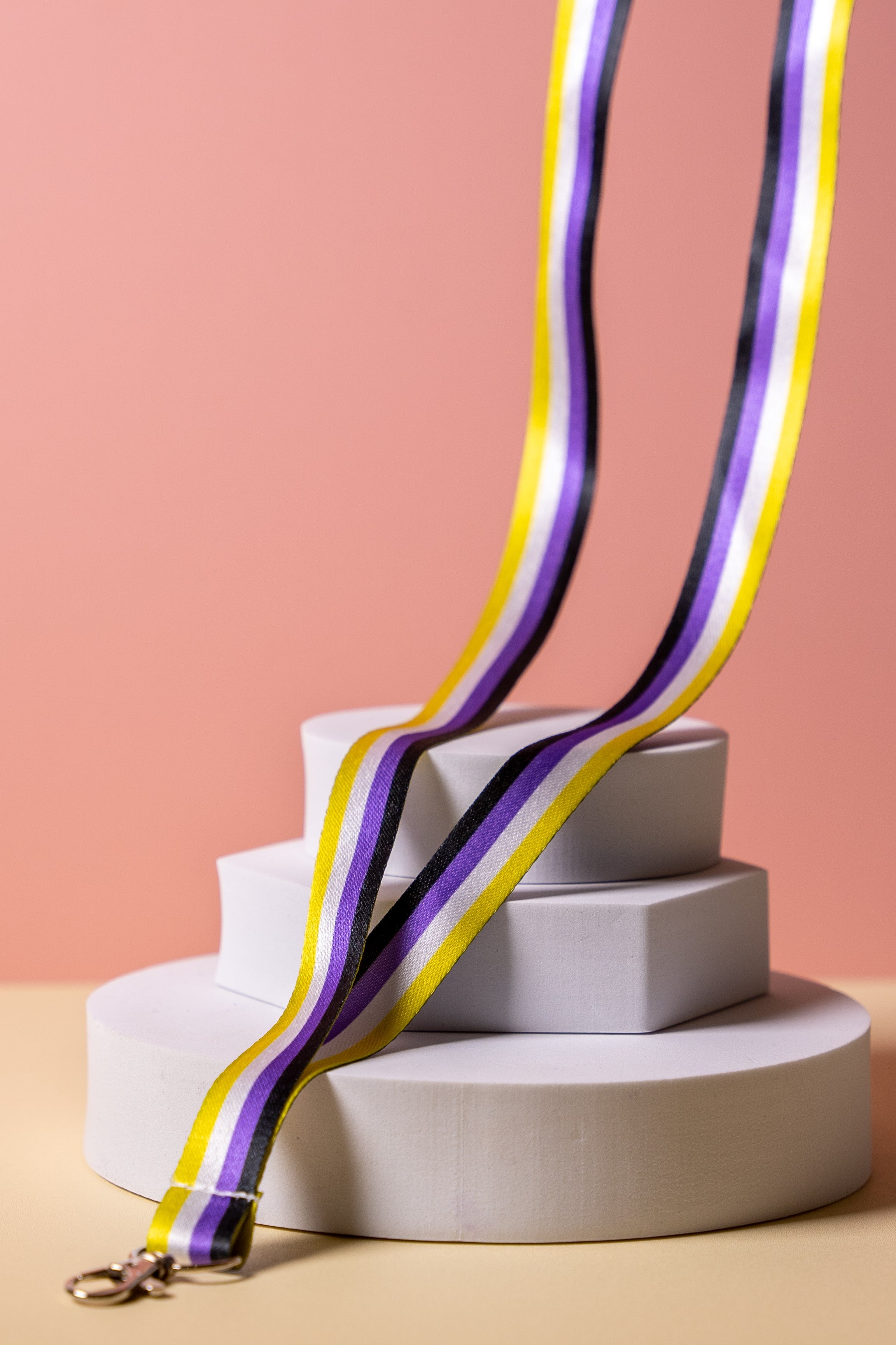 Non binary flag striped lanyard on a white platform with a pink background