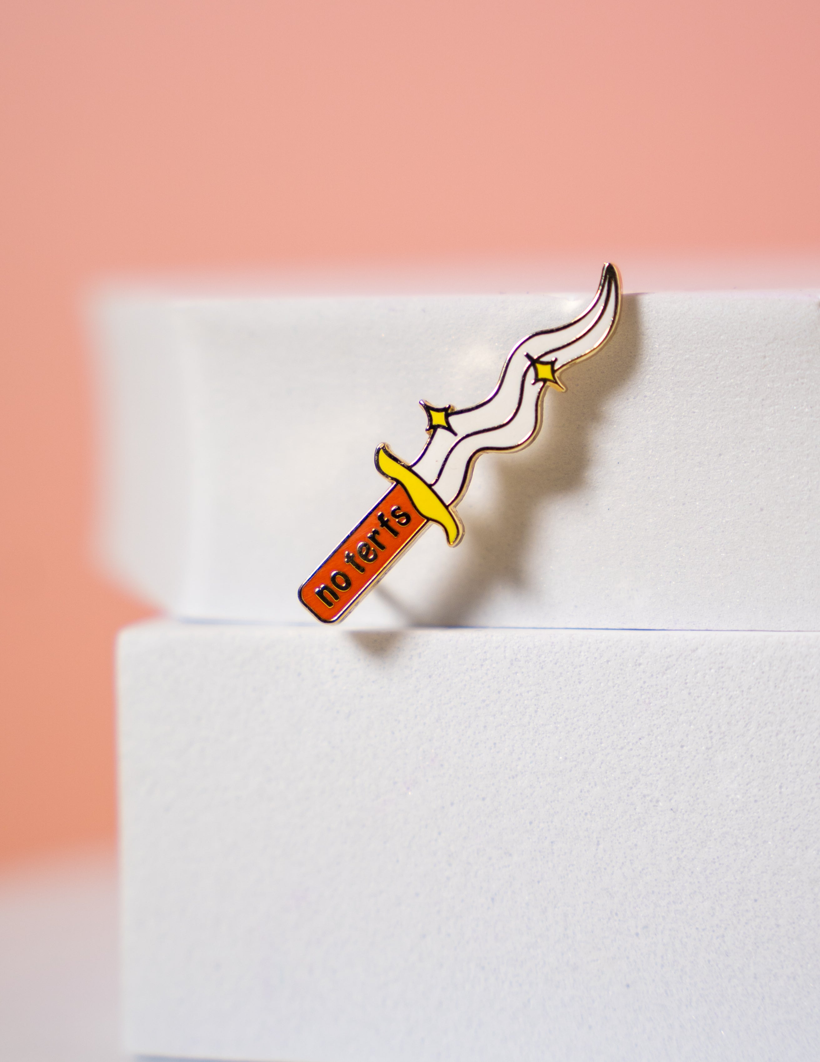 A small pin in the shape of a dagger that reads "no terfs" on the handle.