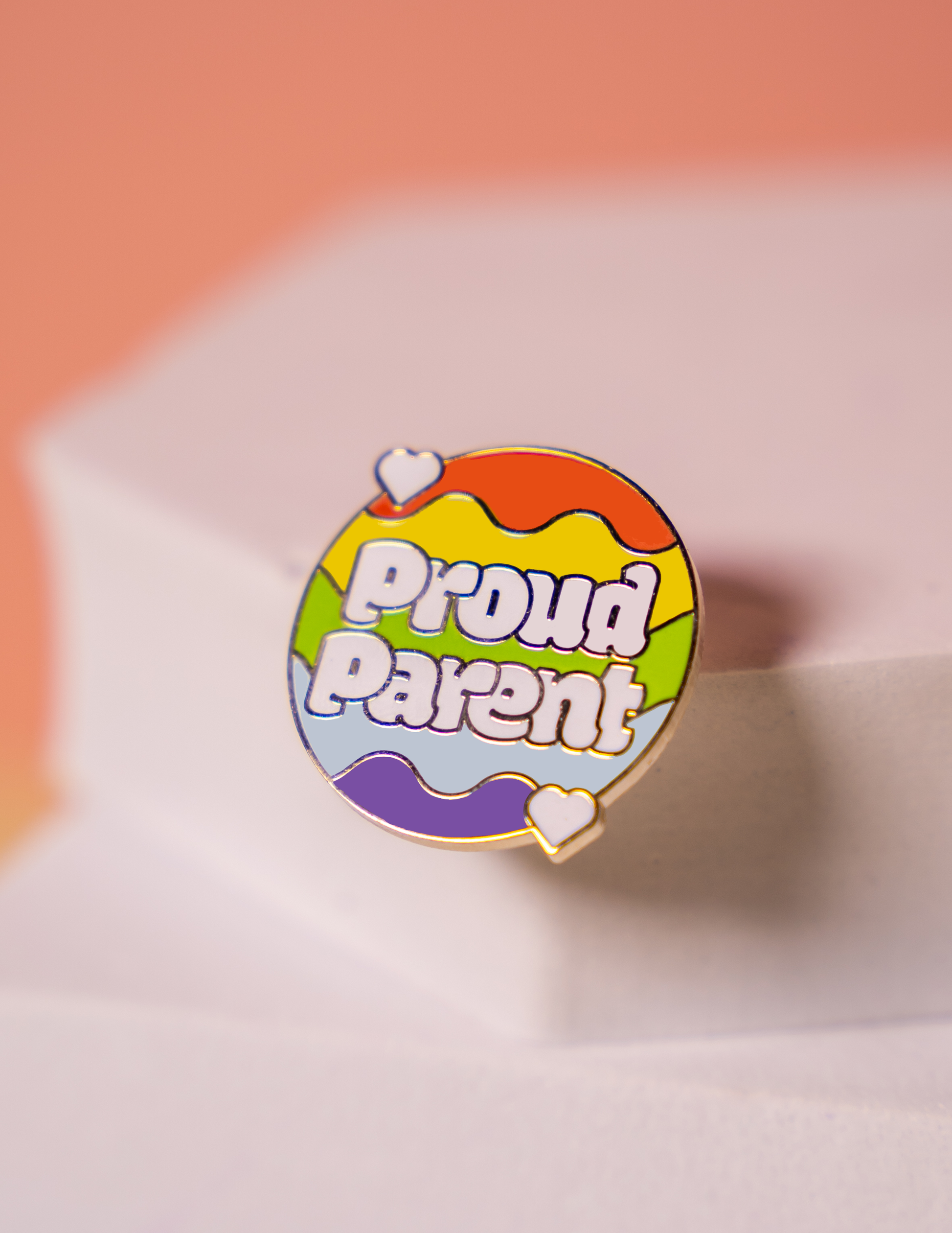 a small pin with a rainbow background reading "Proud Parent"