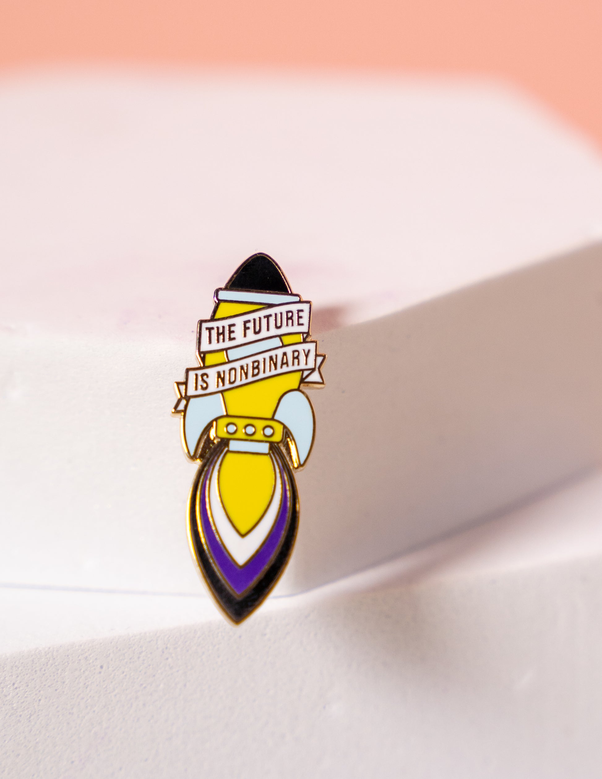 Enamel rocket shaped pin with 'The Future is Nonbinary' message on a white background