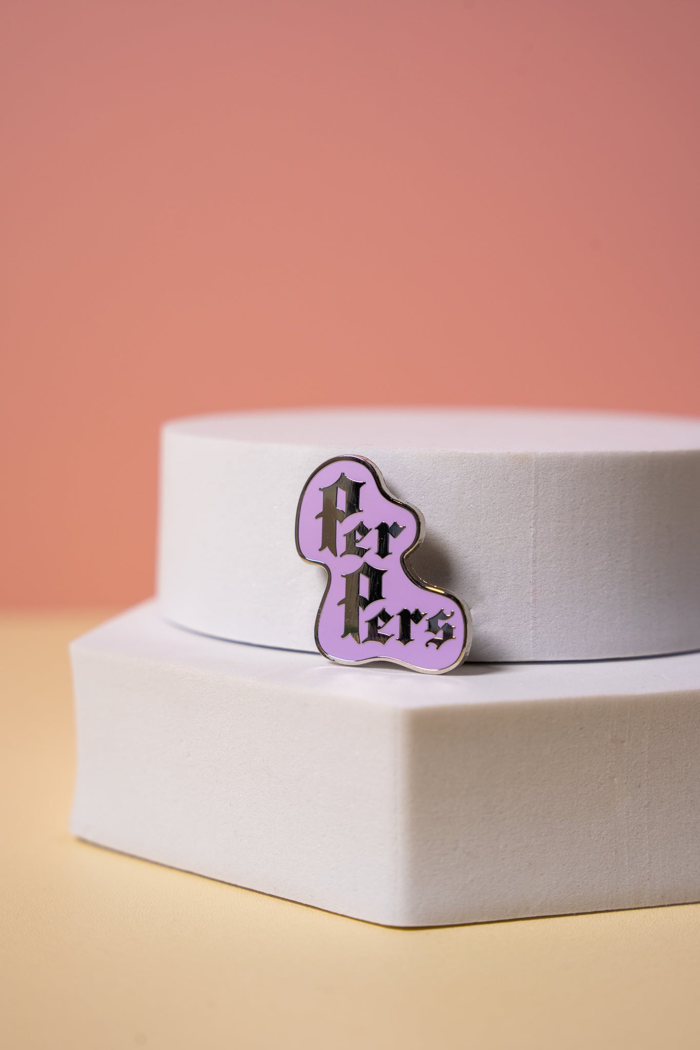 Purple enamel pin with 'Per Pers' text on a white box against a pink background