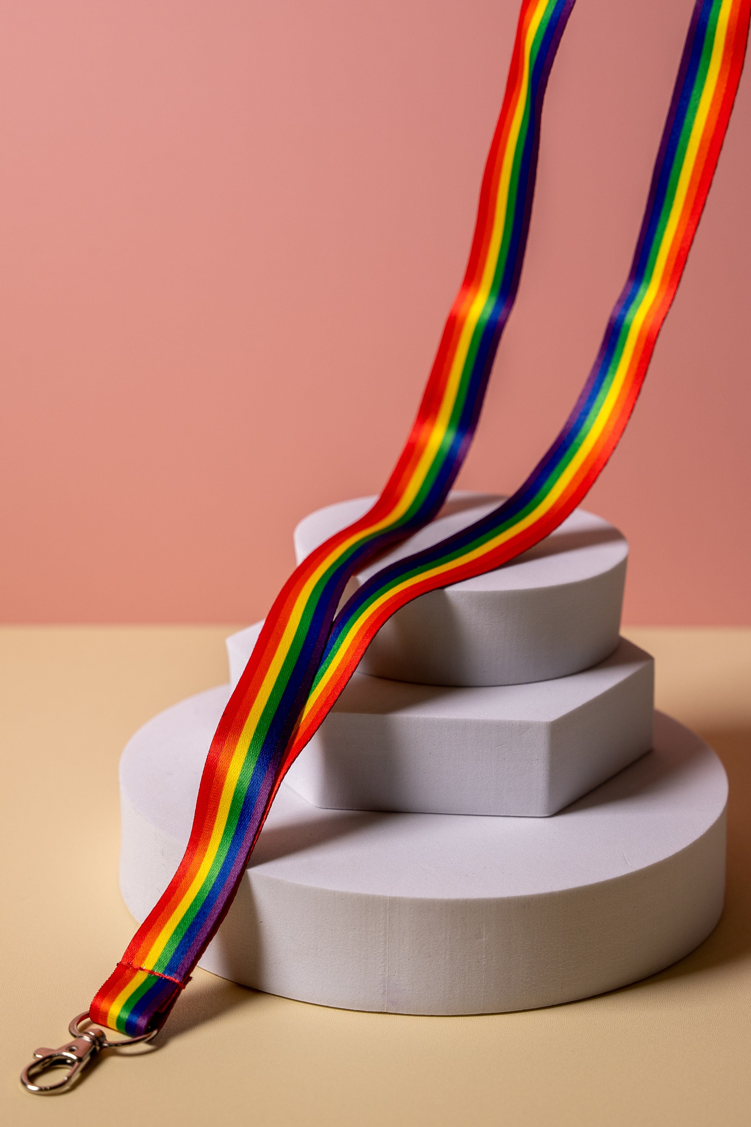 Rainbow striped lanyard on a white cylindrical stand against a pink background