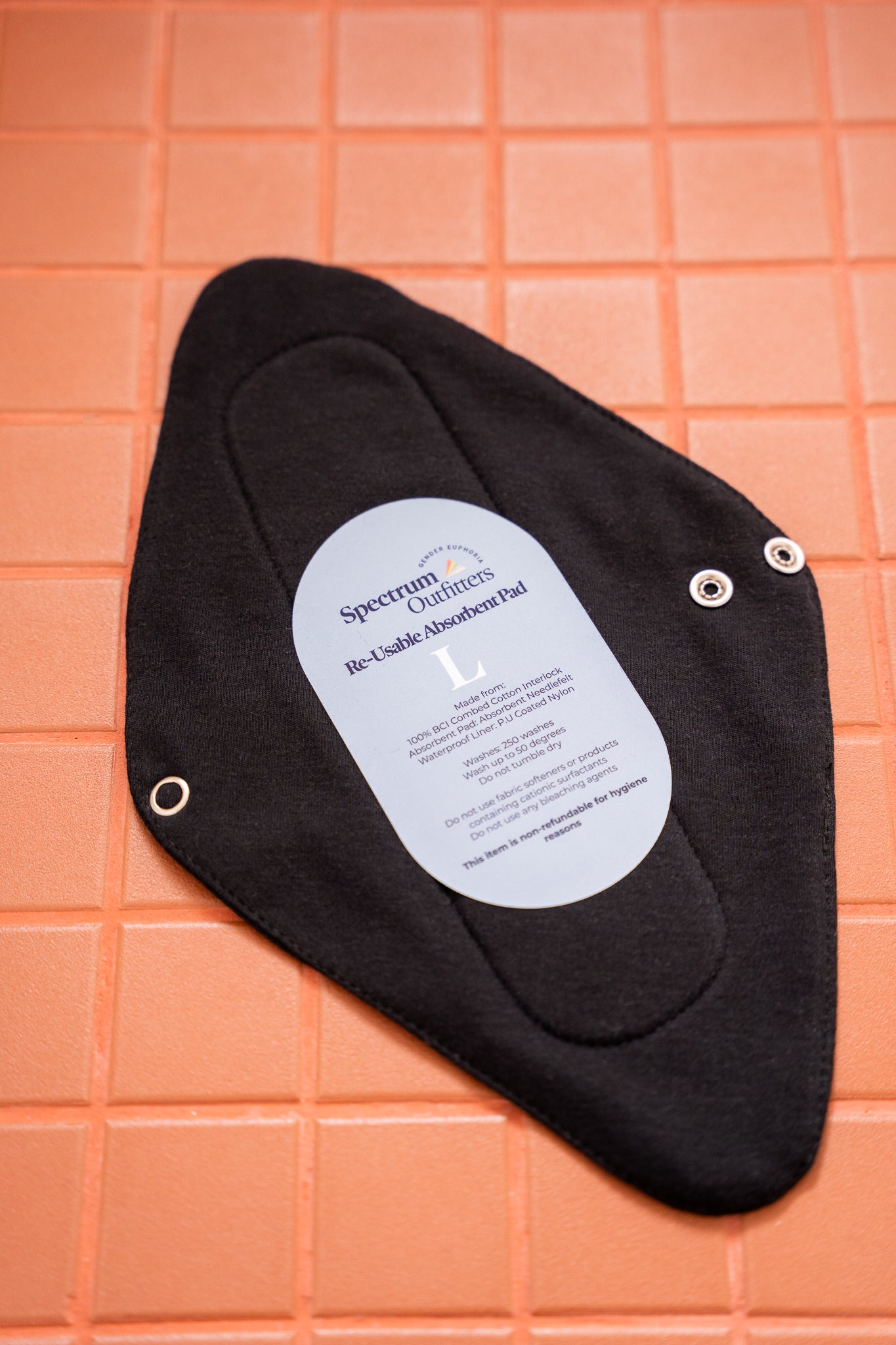 Black reusable menstrual pad with a label on an orange grid background