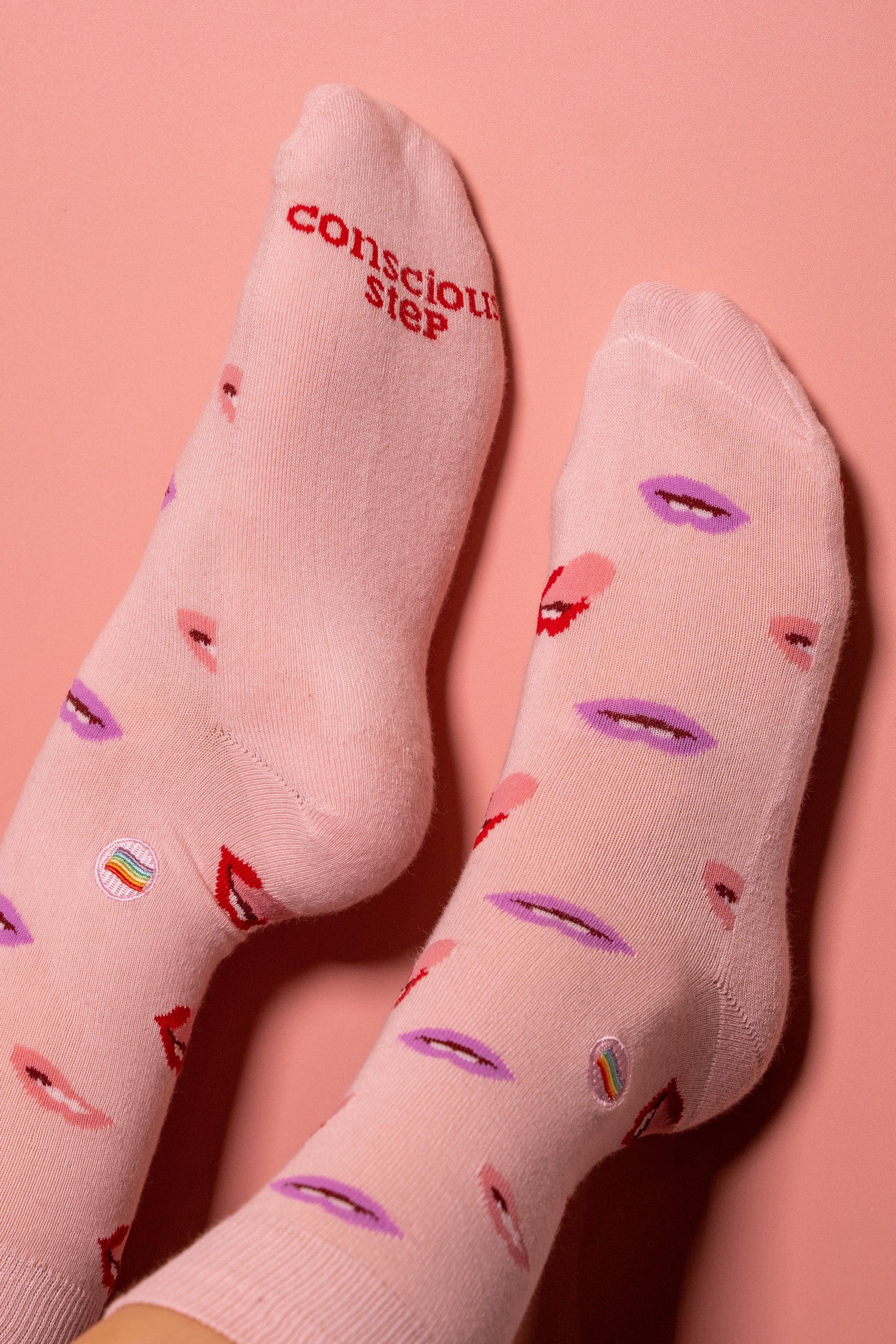 Pink socks with lip print and 'Conscious Step' text on a pink background