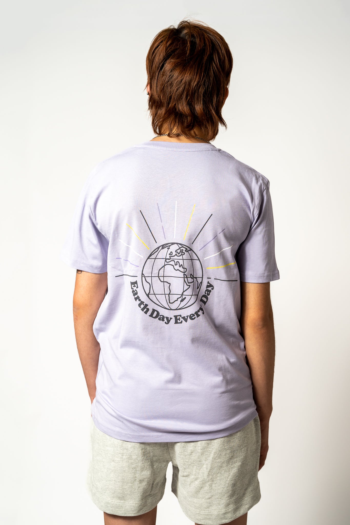 Person wearing a light purple t-shirt with an 'Earth Day Every day' graphic print on the back, standing against a white background.